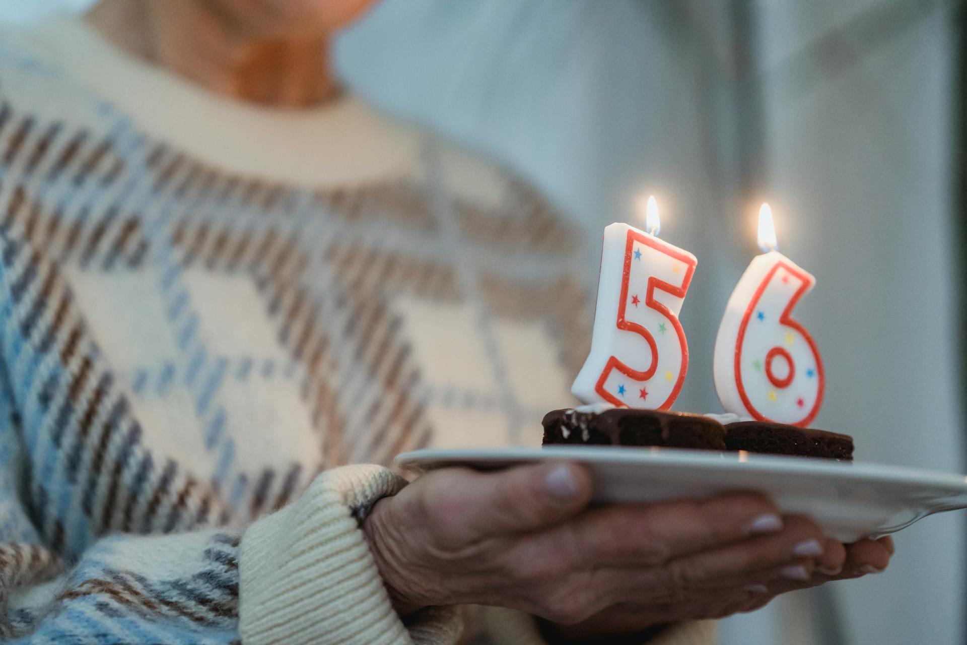 Crop anonymous middle aged female holding plate with delicious baked treats and flaming number candles on birthday