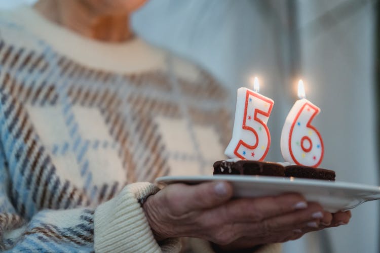 Crop Mature Woman With Burning Number Candles On Muffins