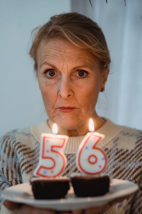 Mature woman with delicious muffins and burning number candles