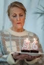 Mature woman in sweater holding plate with tasty chocolate desserts and burning number candles on birthday