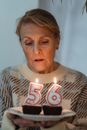 Mature female in cozy sweater holding plate with delicious birthday cakes and burning candles in shape of numbers