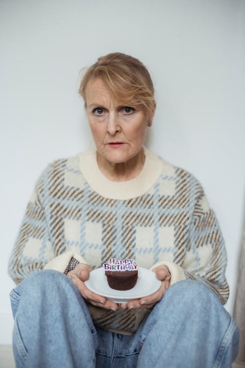 Serious mature woman holding birthday cupcake and sitting on floor