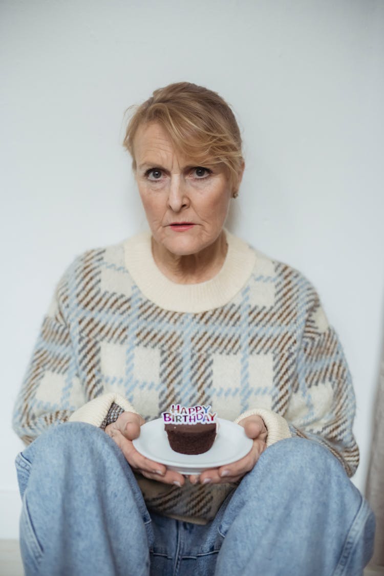 Serious Mature Woman Holding Birthday Cupcake And Sitting On Floor