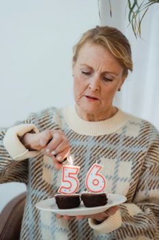Senior female in casual sweater lightning candles in shape of numbers placed on birthday chocolate cupcakes