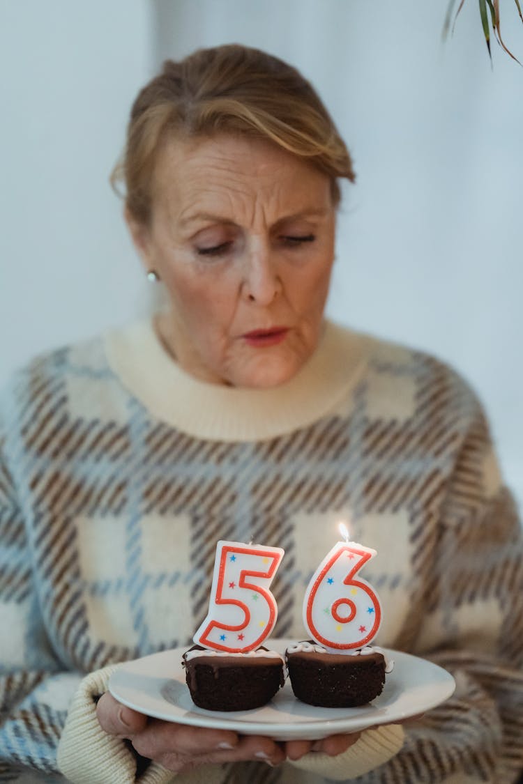 Mature Woman Blowing Candles On Birthday Cupcakes