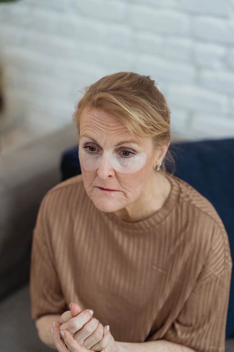 Contemplative Mature Woman With Eye Patches Sitting On Sofa