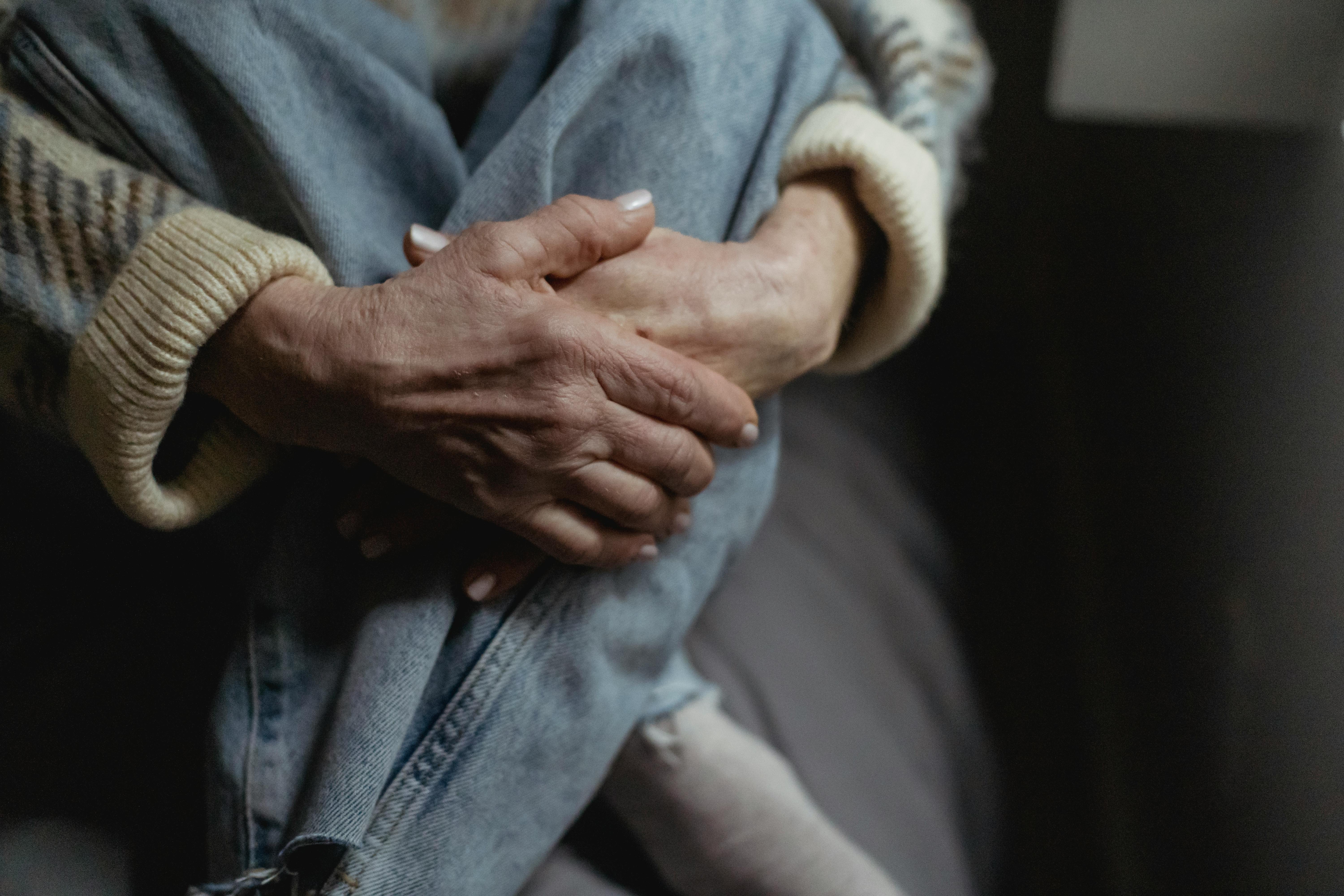 crop faceless mature woman embracing knees on sofa