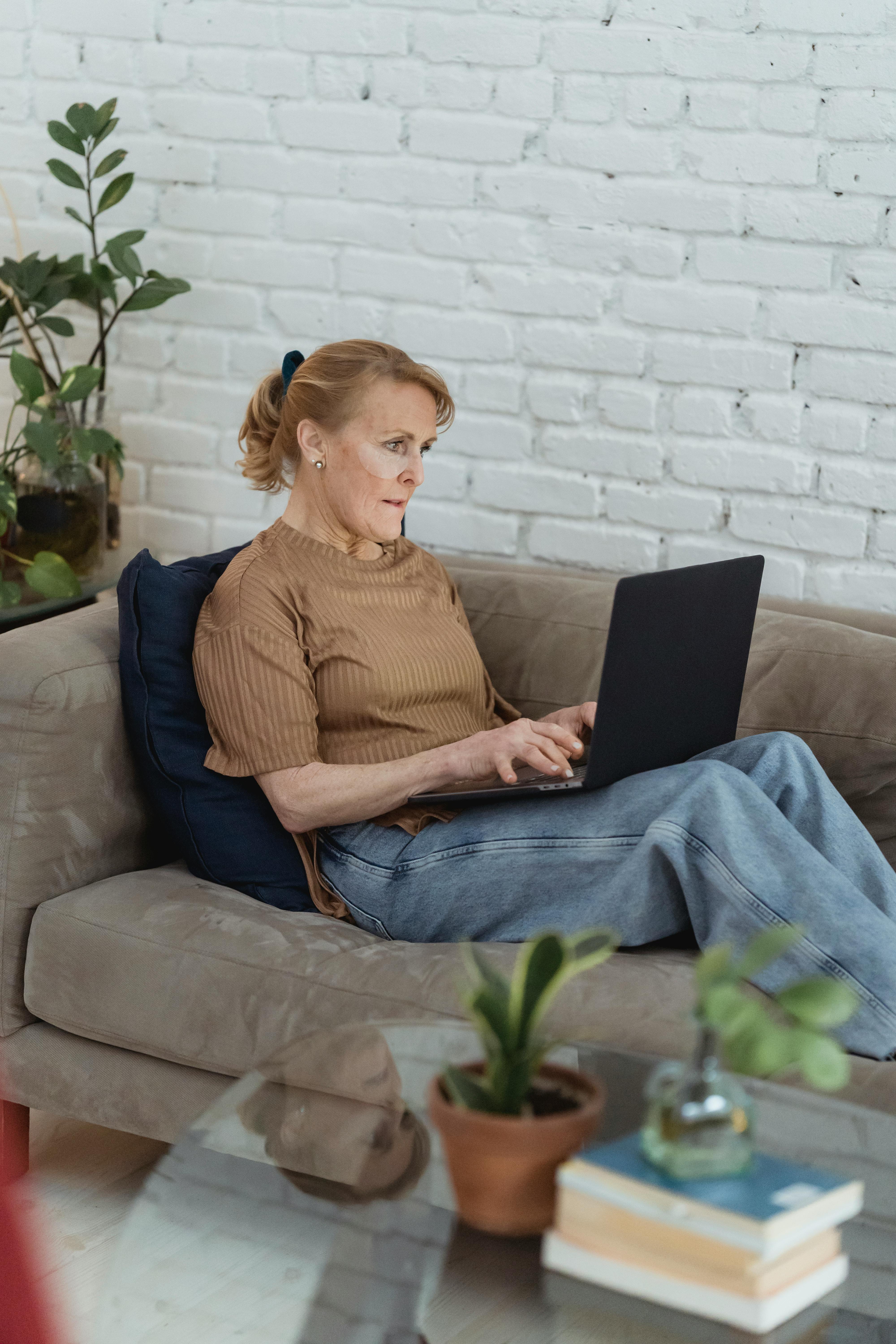 focused mature woman using laptop on sofa