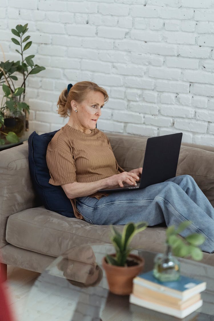 Focused Mature Woman Using Laptop On Sofa