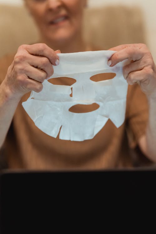 Crop glad mature woman applying moisturizing face mask