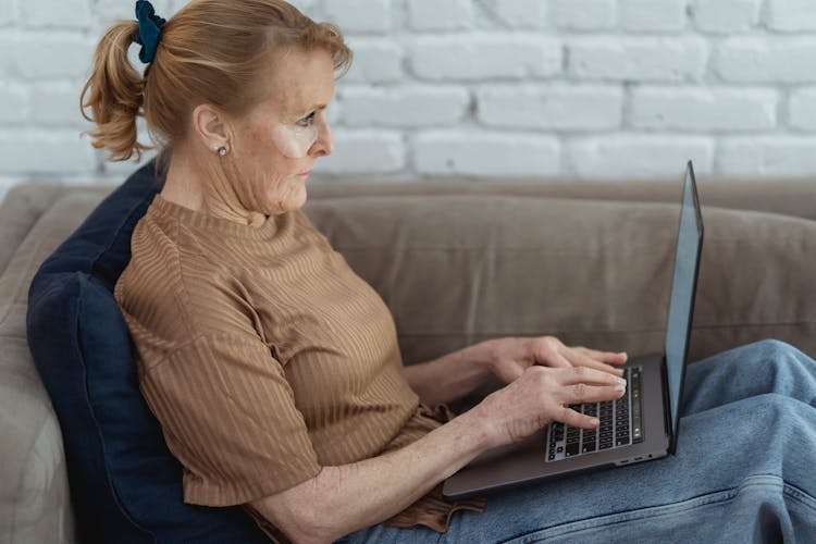 Crop Mature Woman Working On Laptop On Cozy Sofa