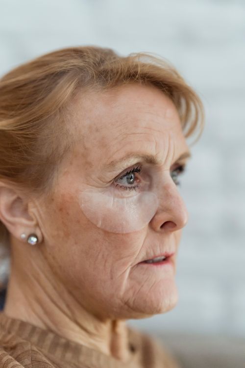 Free Crop contemplative senior female wearing anti aging under eye patches and looking away thoughtfully Stock Photo