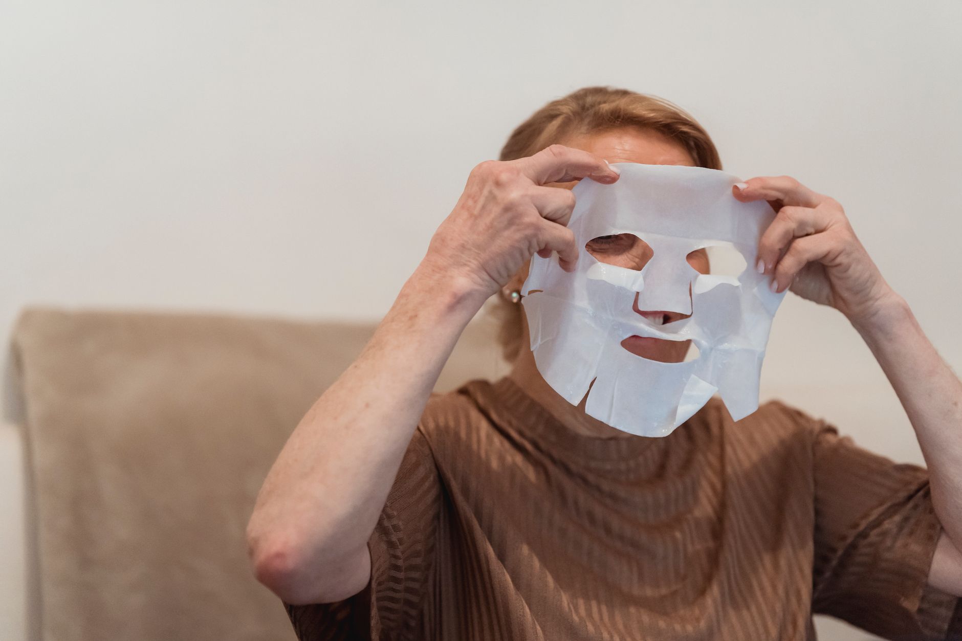 A woman gently applying a Korean sheet mask to her face, showcasing a moment of self-care and relaxation.