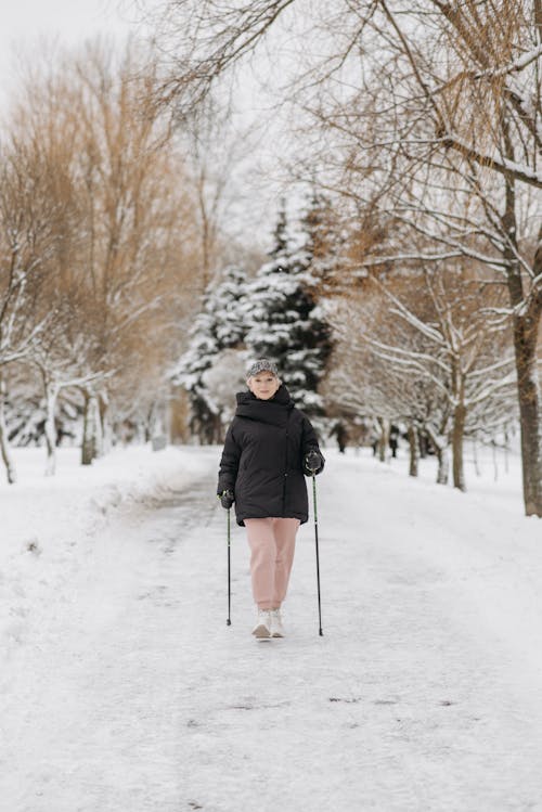 A Woman with Trekking Poles Walking on White Snow