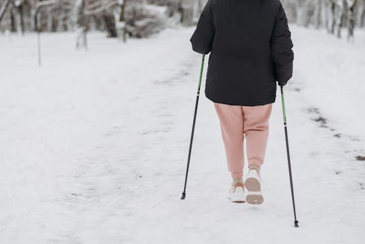 Person walking on snow-covered path with trekking poles in a winter landscape.