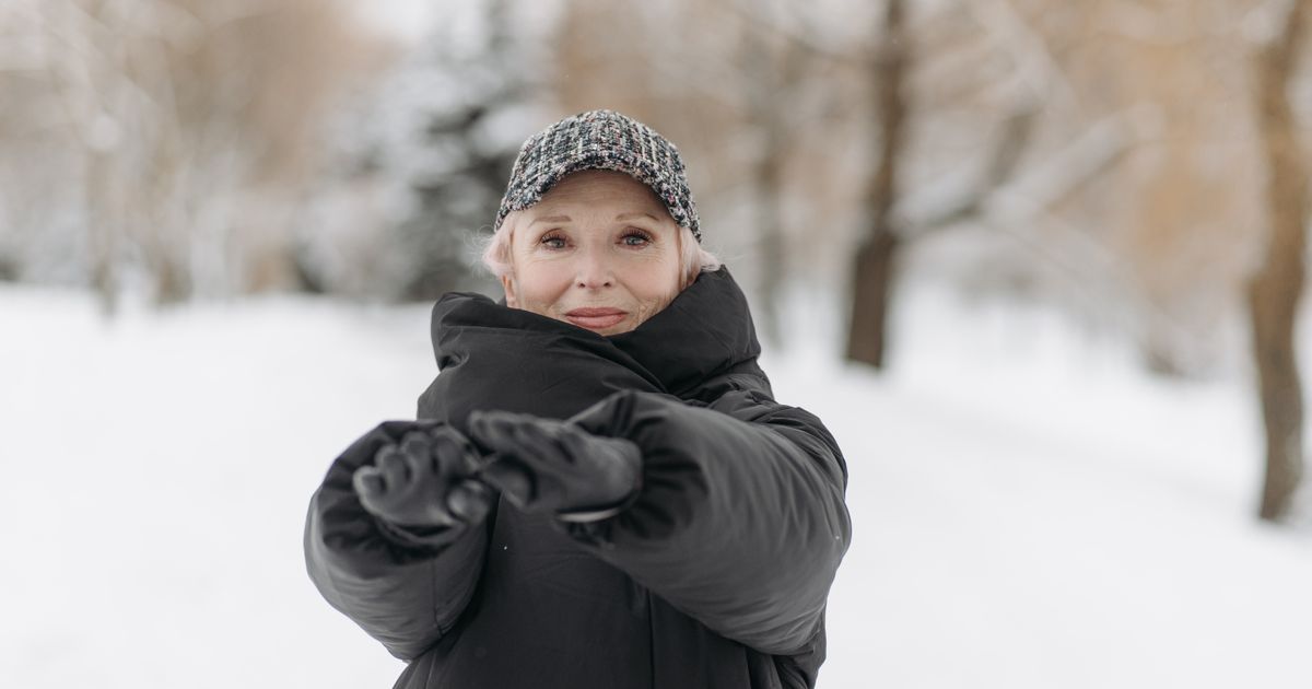 Senior woman in winter clothing stretching her arms outdoors in a snowy park