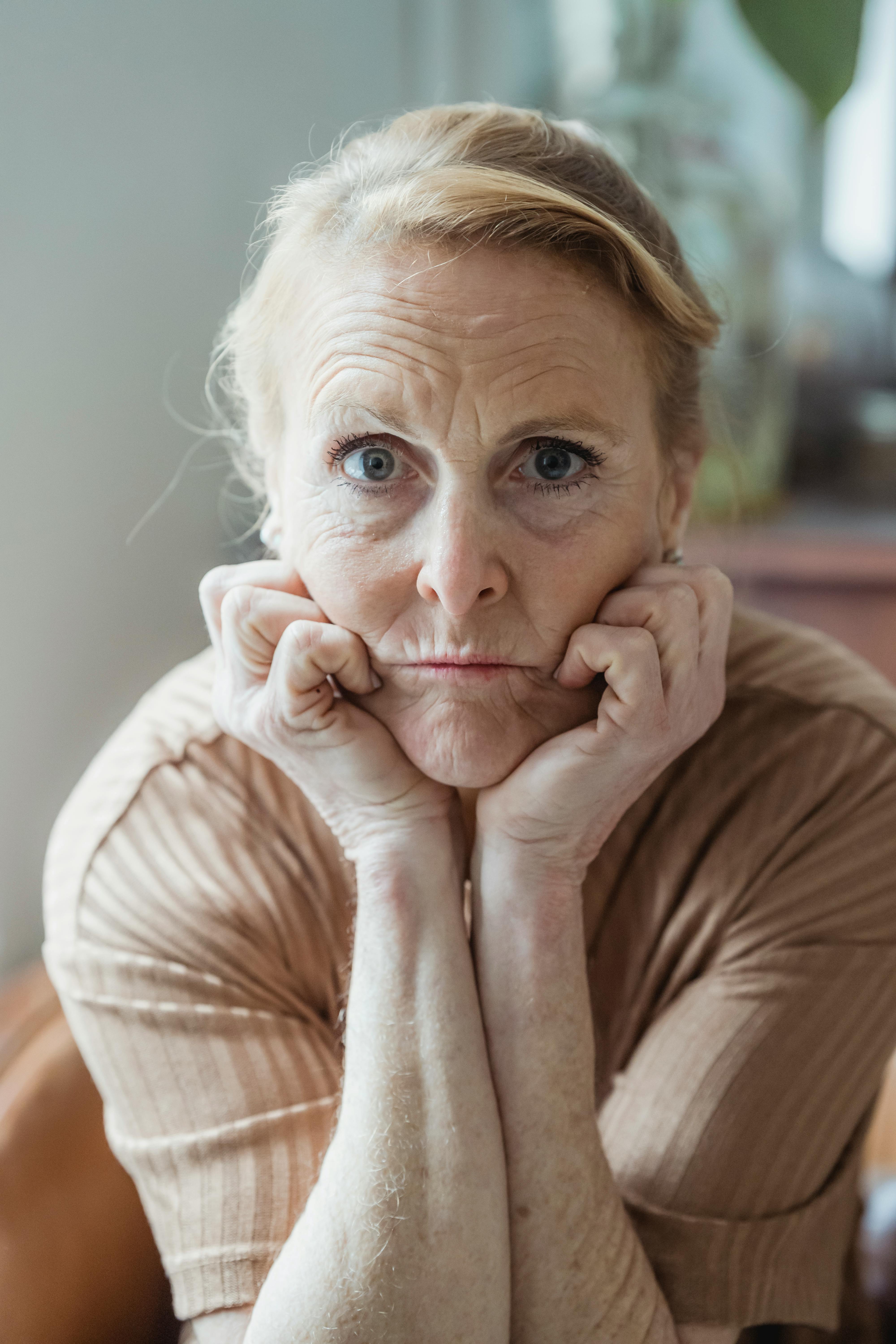 Mature Woman in Brown Shirt with Hands on Cheeks · Free Stock Photo