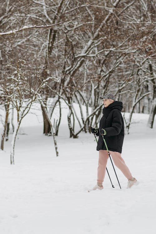 An Elderly Woman with Trekking Poles Near Bare Trees