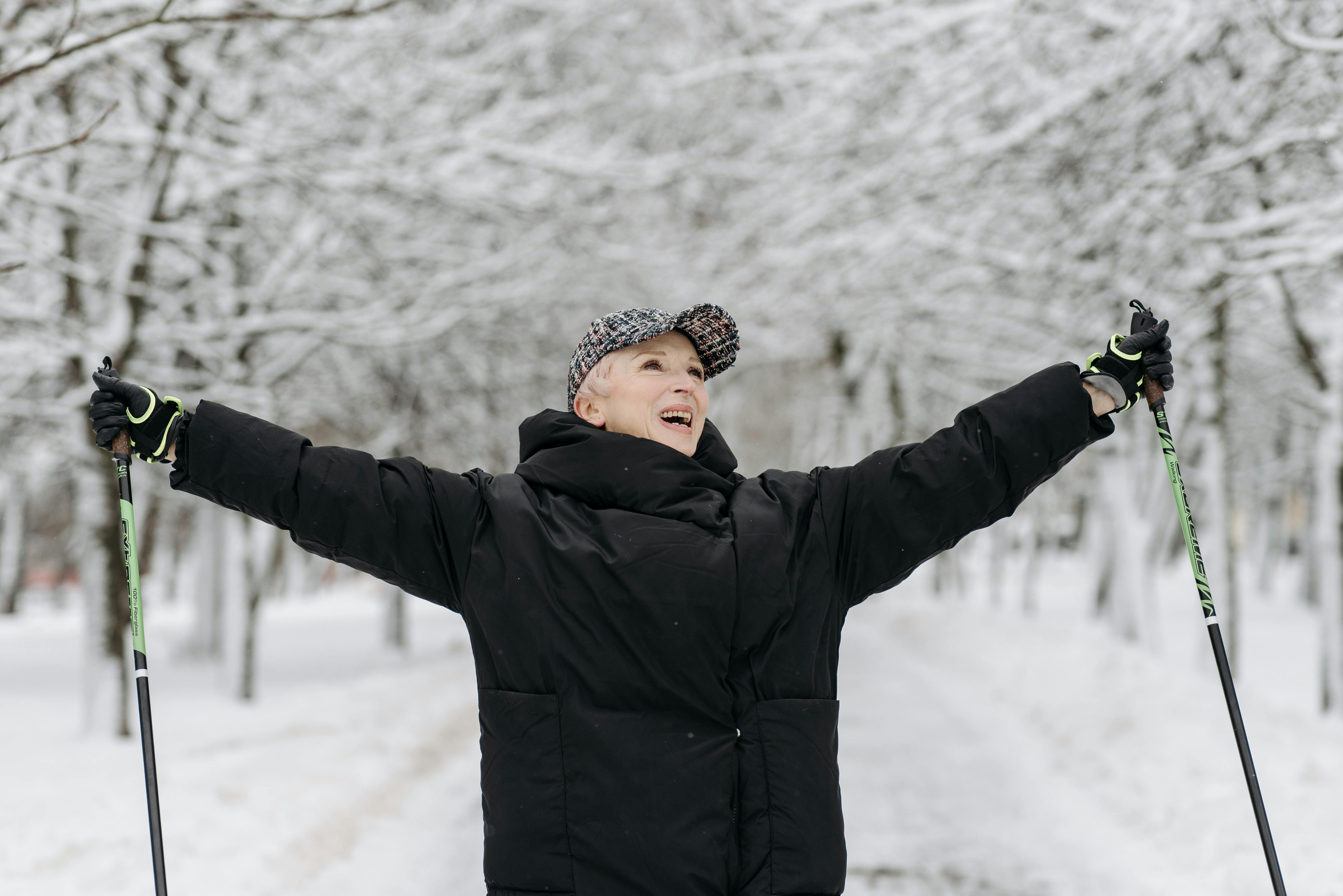 Prescription Goggle Inserts - Senior woman celebrates with raised arms while skiing in a snowy park, exuding joy and freedom.