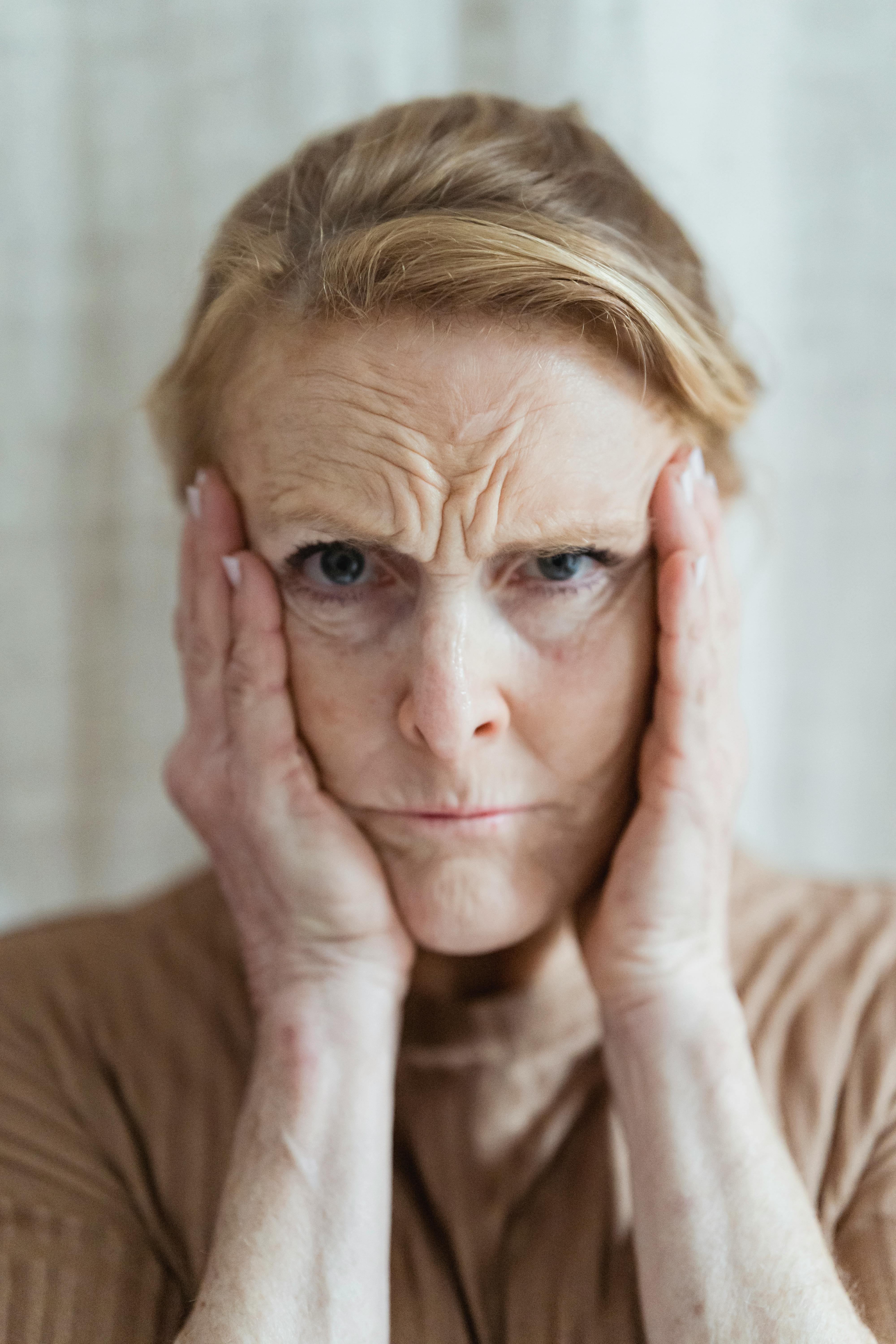 woman wearing a brown shirt with hands on face