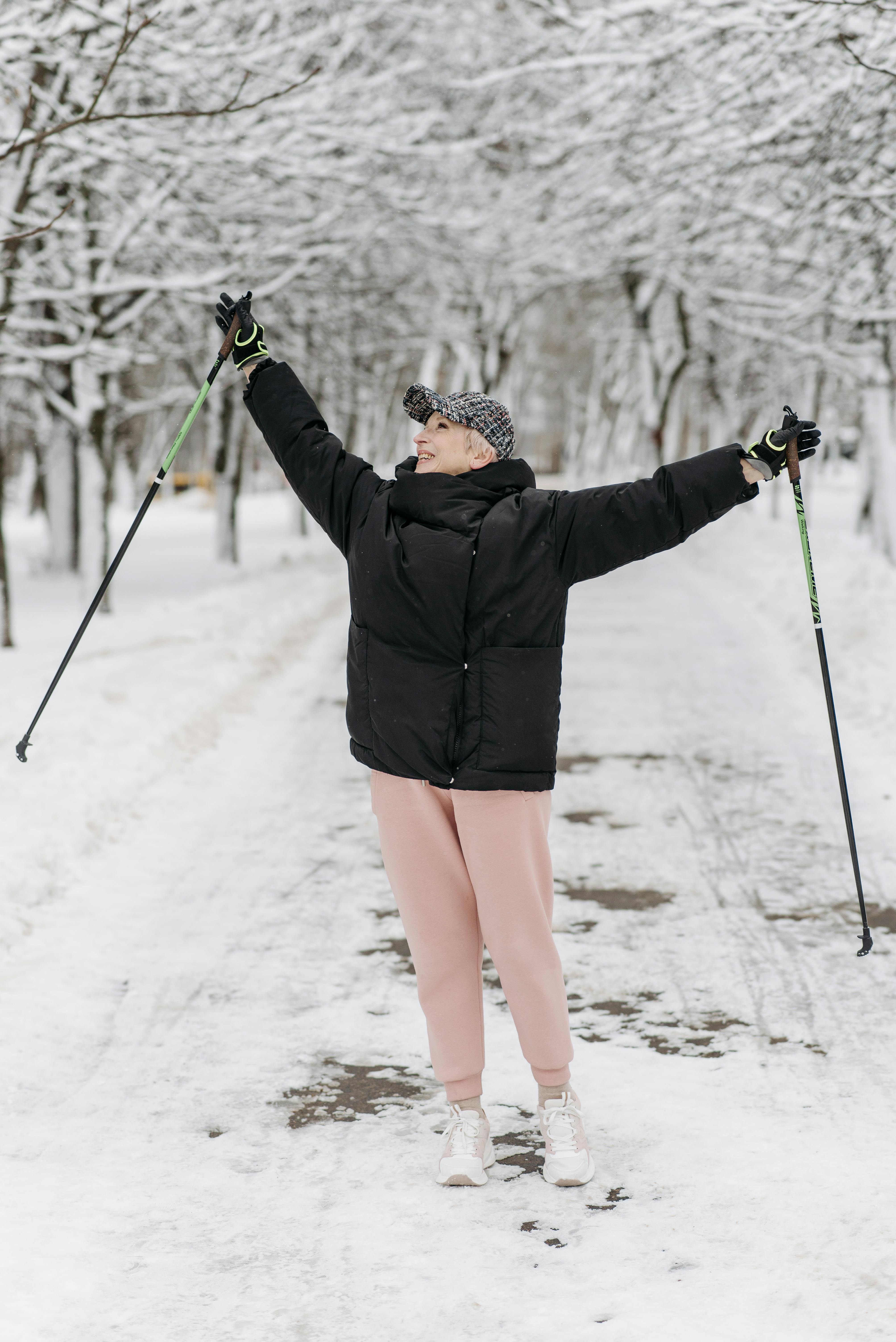 woman in a black jacket raising her arms while holding trekking poles