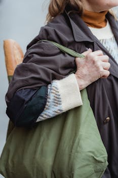 Close-up of a woman holding a green bag with a baguette handle showing outdoors.