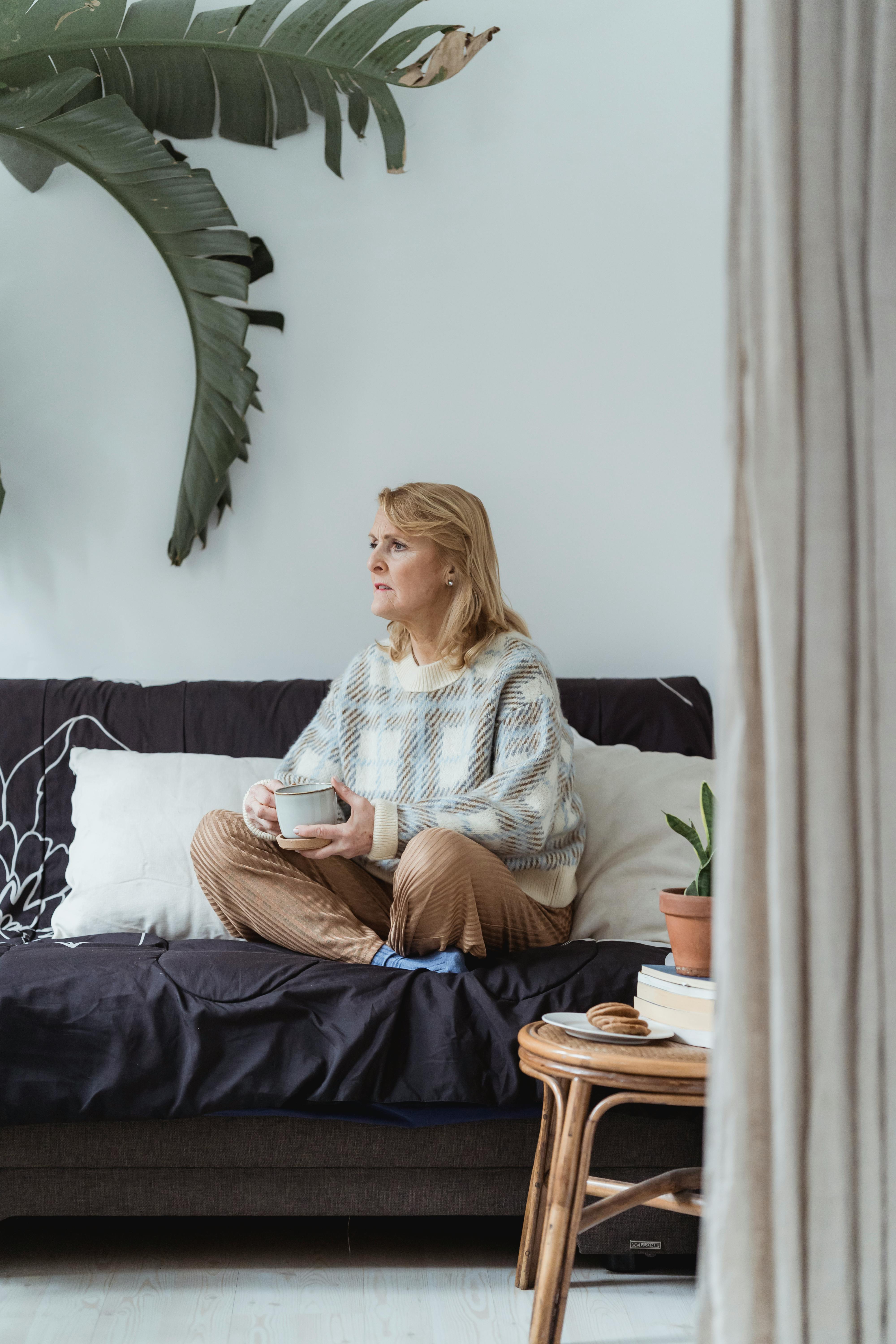 photo of an elderly woman holding a cup while sitting on a sofa