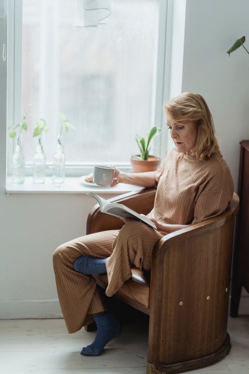 Free Elderly woman enjoying coffee and reading in a cozy chair by the window. Stock Photo