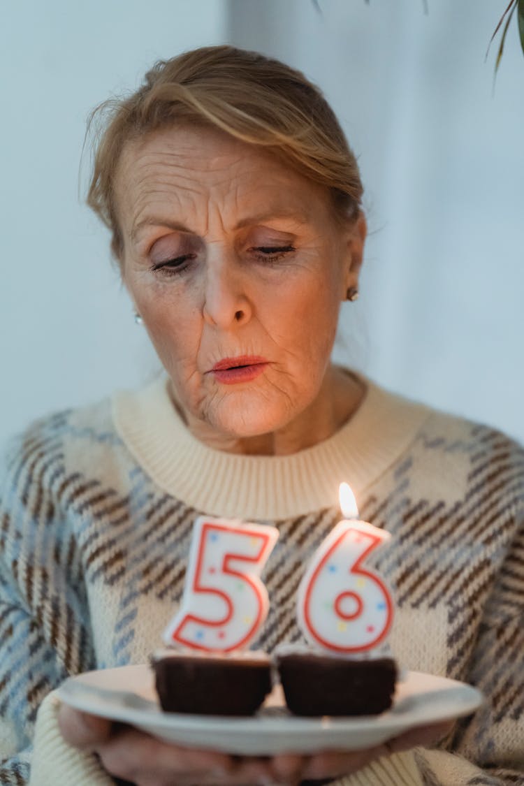 Mature Woman Blowing Candles On Birthday Cupcakes