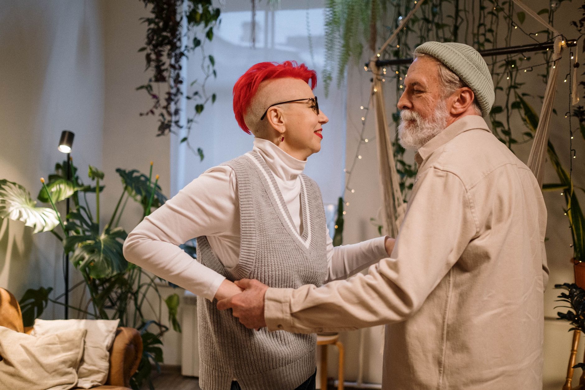 Elderly couple dancing together in a cozy living room surrounded by plants.