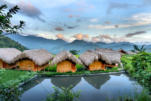 Tranquil rural landscape featuring straw huts by a serene retention pool with mountains in the background.