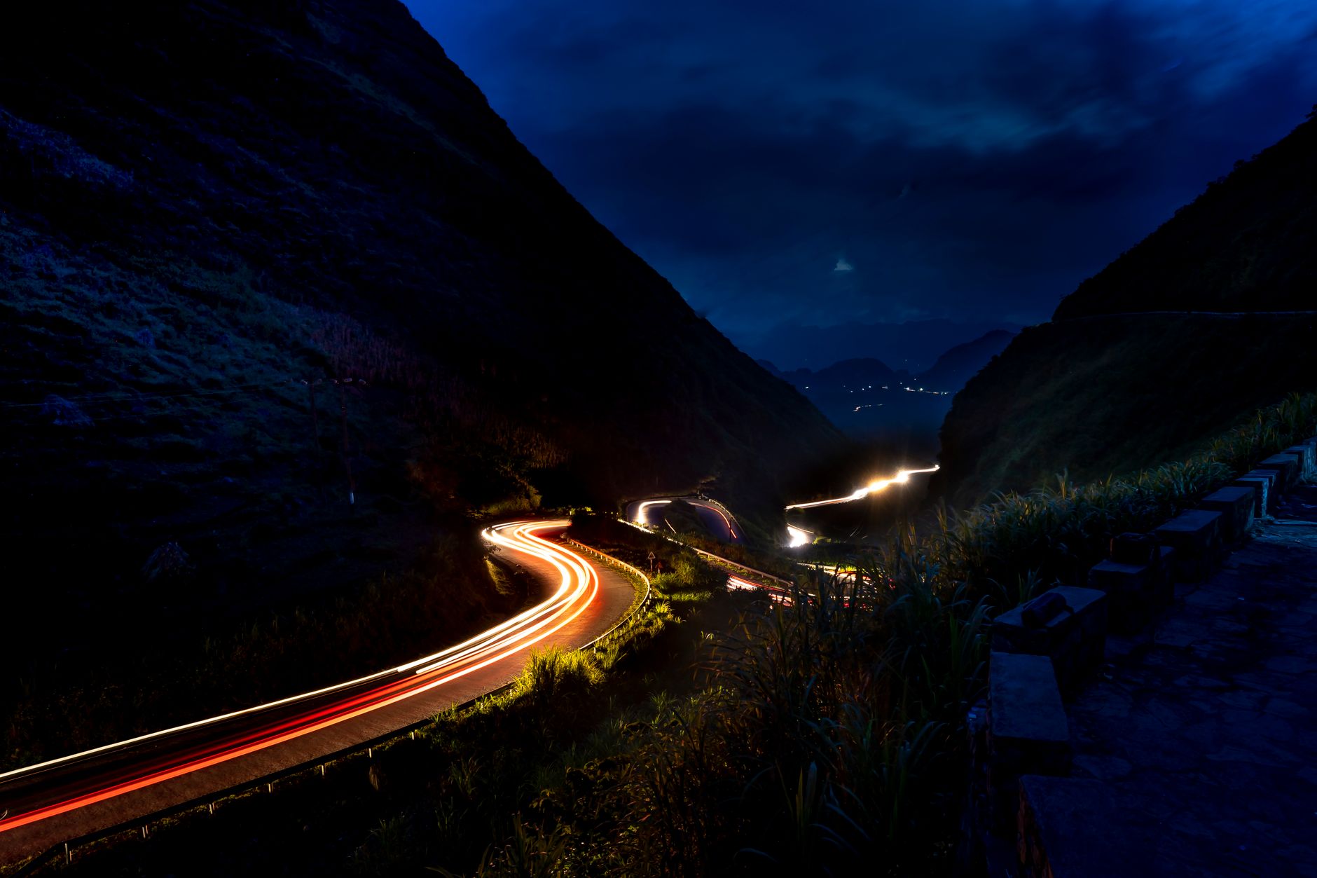 Illuminated mountain road with curving light trails under a dark night sky.