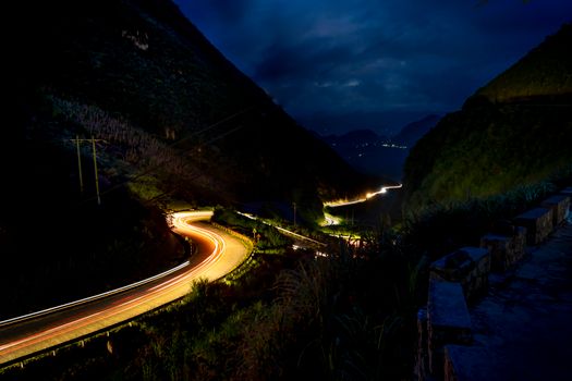 Captivating nighttime mountain road scene with vibrant light trails and a dramatic night sky.