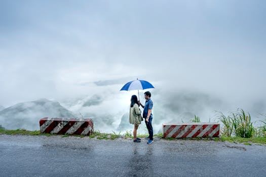 A couple standing with an umbrella on a misty cliff road surrounded by concrete barriers.