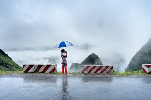 A Woman Under an Umbrella Taking Photos of the Scenery