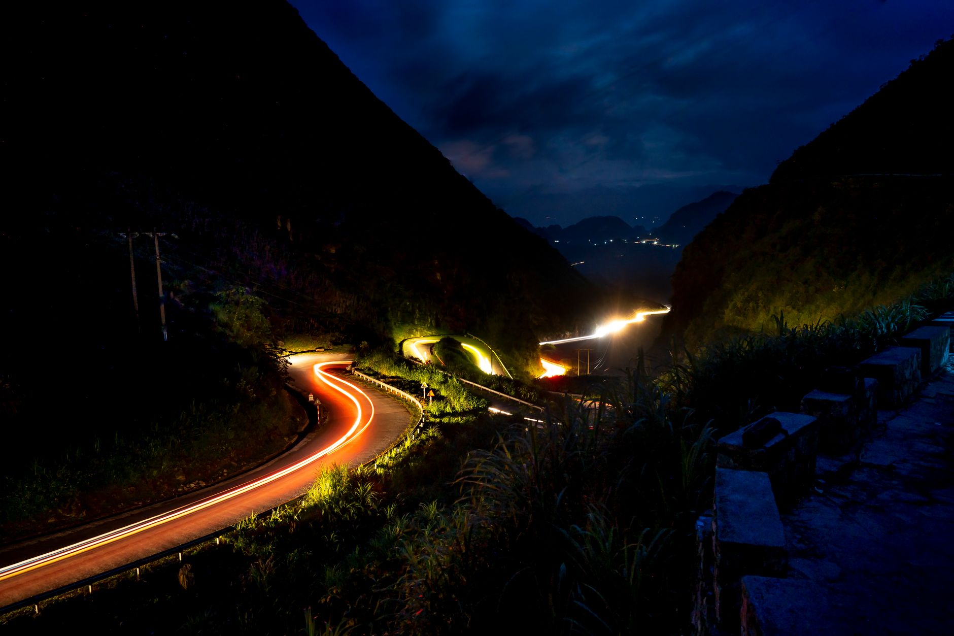 Stunning night view of a winding mountain road with vibrant car light trails under a starry sky.