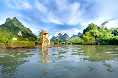 Man in Conical Hat in Water in Mountain Landscape