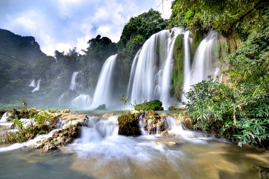 Stunning long exposure of a large waterfall cascading in a lush tropical setting.