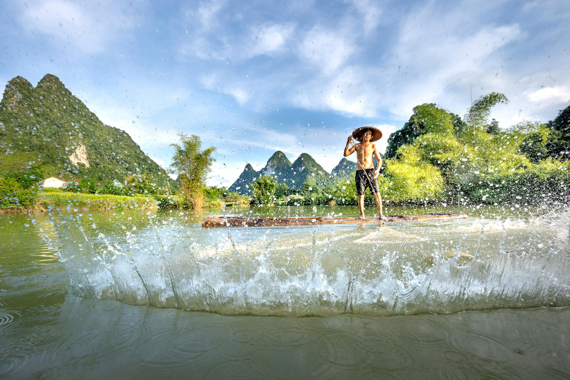 Man fishing with a net in an idyllic Chinese landscape with mountains and water splash.