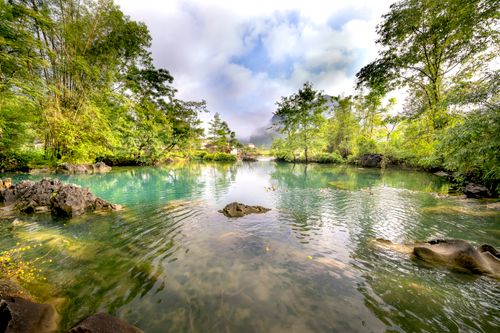 Free Serene tropical lake with crystal-clear water and lush green forest, ideal for nature lovers. Stock Photo