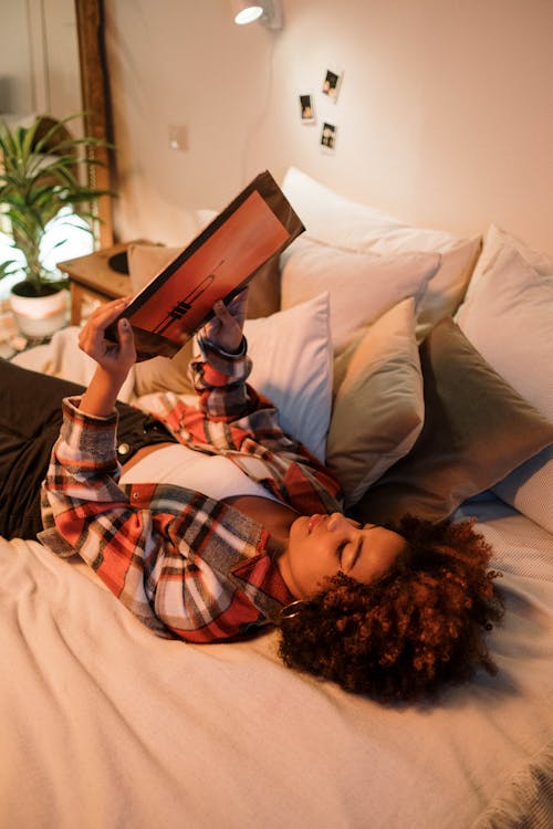 Photo of a Woman Lying on a Bed while Holding a Vinyl