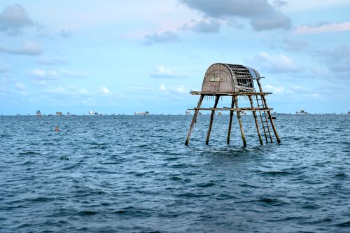 Free A dilapidated stilt house stands alone in the calm ocean, under a cloudy sky. Stock Photo
