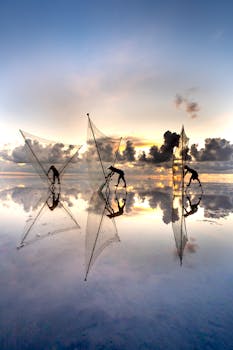 Three fishermen casting nets, reflected in the calm water at sunrise.