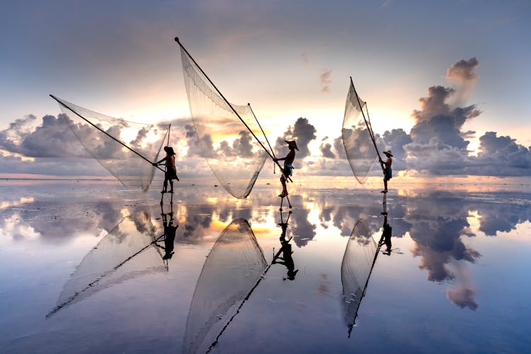 Men Throwing A Fishing Net In Sea At Dusk 