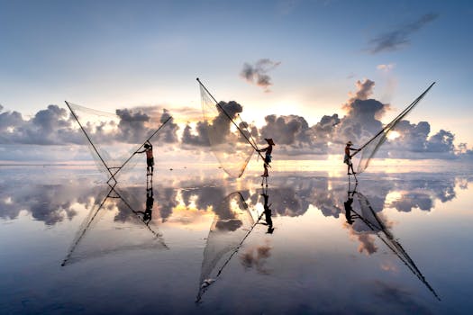 Silhouetted fishermen casting nets at sunrise on a reflective seashore.