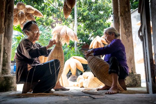 Senior artisans skillfully crafting traditional bamboo baskets in a serene, sunlit setting.