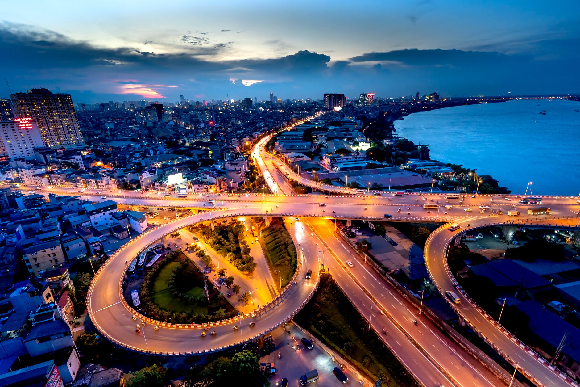 A dramatic aerial view of a city interchange at dusk, showcasing vibrant urban night lights and bustling traffic flows.