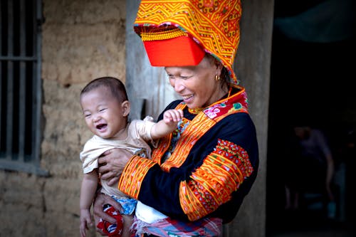 Free Woman in Traditional Decorative Clothing Holding a Baby in front of a House Stock Photo