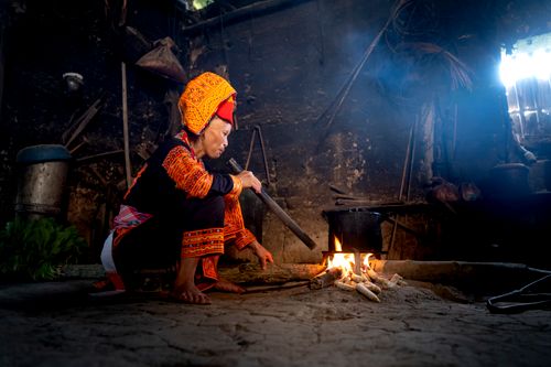 Free A Vietnamese woman in traditional attire cooks over an open fire indoors, highlighting cultural heritage. Stock Photo