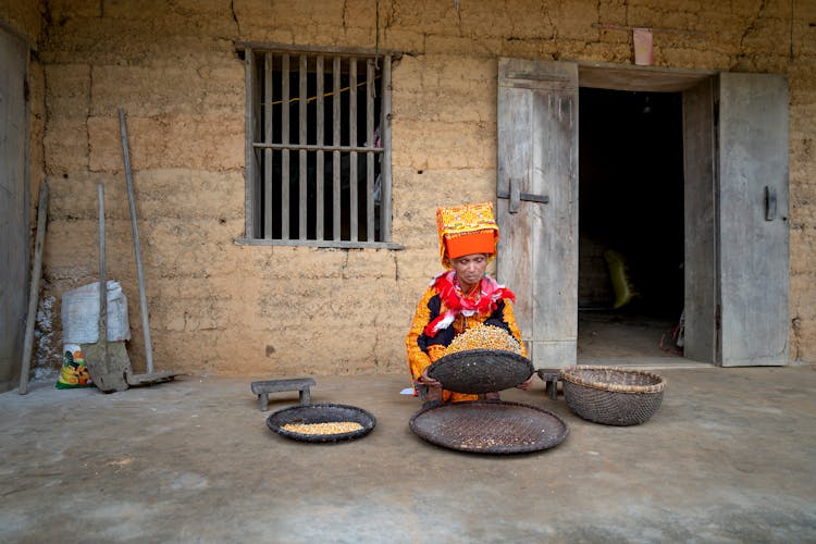 Dao Lu Gang Woman Tossing Food In A Bowl In Front Of A House 